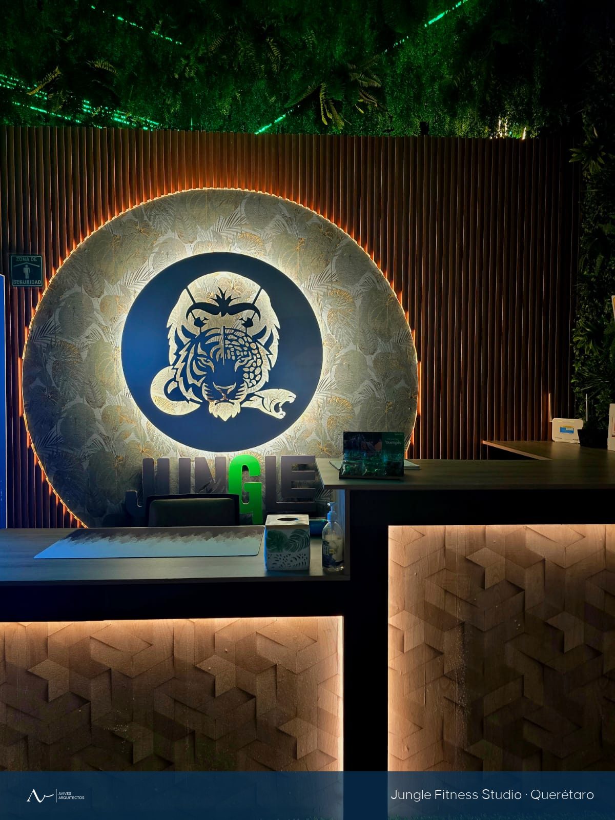 Recepción del gimnasio con logotipo retroiluminado, lambrín de madera y muro vegetal